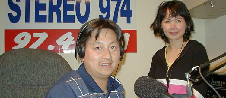 Two broadcasters in studio at 97.4 3WRB. Smiling into camera - one is wearing headphones and sitting in front of a microphone.