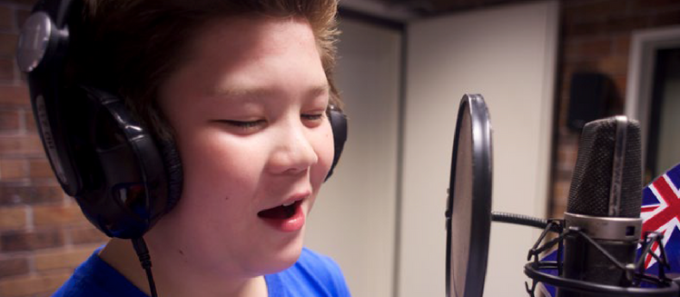 Young boy wearing headphones talking into a microphone. Small Australian flag on display behind microphone.