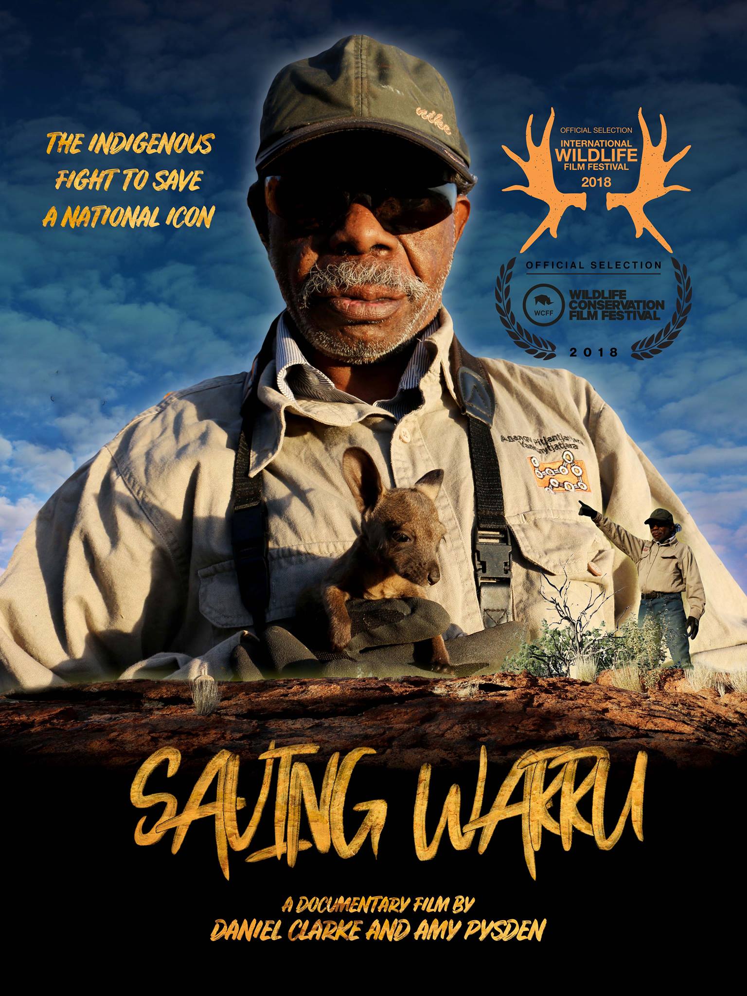 Indigenous man holding small black-footed rock wallaby against blue cloudy sky. Writing - The Indigenous fight to save a national icon. A documentary film by Daniel Clarke and Amy Pysden. Official selection International Wildlife Film Festival 2018. Official Selection Wildlife Conservation Film Festival 2018.