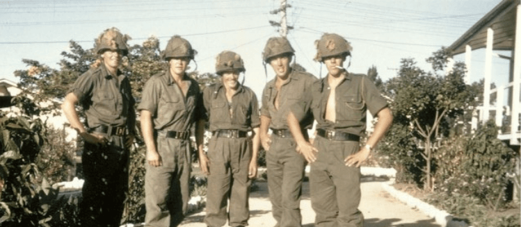 Group of five soldiers in uniform standing outside grouped together 