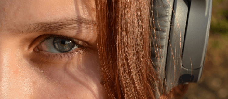 Close up of an auburn-haired woman's left eye with black headphones
