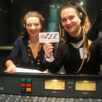 A woman and man wearing headphones in the Radio 3ZZZ studio holding a small ZZZ signstudios 