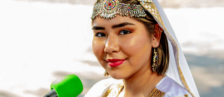 Woman wearning ornate head scarf speaks into green microphone smiling at camera