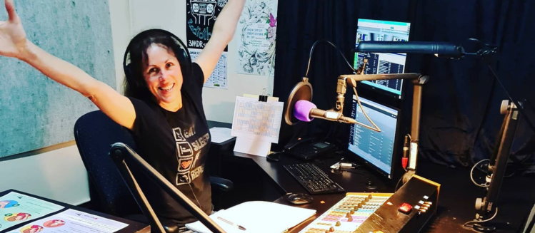 Lady in studio with headphones and smiling with wide spread arms