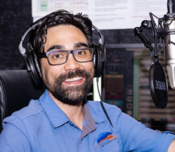 Man with blue collared shirt with glasses dark eyes and dark hair in the studio with headphones