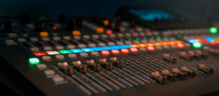 Sound desk console in the dark with buttons lit up and faders