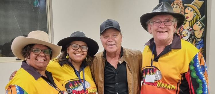 Three people in yellow polo tops and wide brim hats standing next to a man with a black cap and brown leather jacket