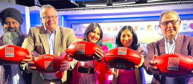 Five people holding red footballs posing in a television news studio in front of a screen