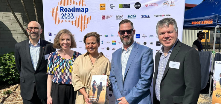 A group of five people standing side by side outdoors in front of a media wall featuring the words Roadmap 2033