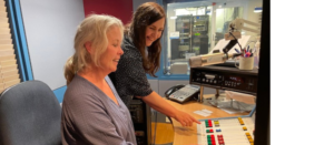 Two women smiling and looking at a mixing desk, owiht one pointing something out to the other