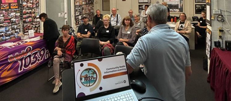 An audience watching a presentation inside a beige cream room with a laptop on a lectern