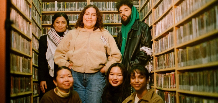 Three young people standing side by side in an archive room filled with shelves of CDs